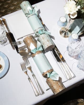 A table is laid for a feast, with crystal glasses, crackers in duck-egg blue and a plate of petit fours, seen from above.