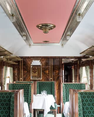 interior of cygnus train carriage with a pastel pink ceiling, green patterned angular chairs and glossy wood marquetry
