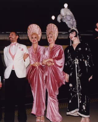 A line-up of five female performers in Art-Deco gowns and headdresses and three men in black, white and pin-stripe suits.