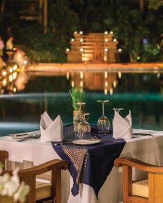 Table for two overlooking a candlelit pool glittering in evening light