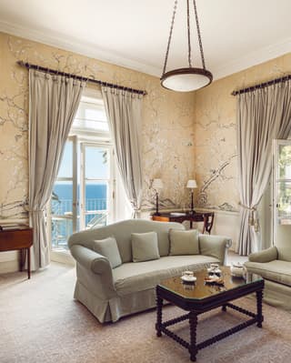 A sage sofa suite and coffee table take centre stage in a grand living room with two balconies and views of sea and gardens.