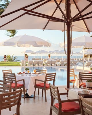 Linen-topped tables under sun umbrellas on a poolside restaurant terrace