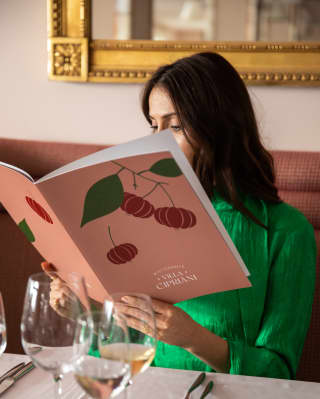 A dark-haired woman in a green top browses the Villa Cipriani menu at a dining table with white wine.