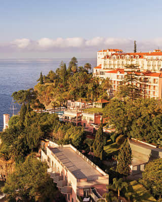 Aerial view of a grand cliffside hotel set among lush tropical gardens