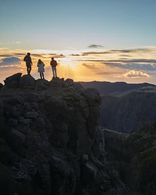 Silhouette of three people standing at a mountaintop above the clouds at sunrise