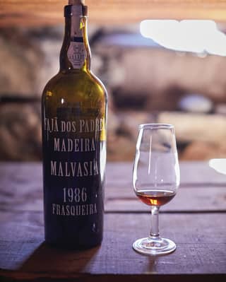 Close-up of a bottle of Madeira wine next to a glass containing a small amount of wine