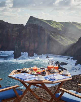 Octagonal table laden with breakfast dishes next to a rugged sea cove