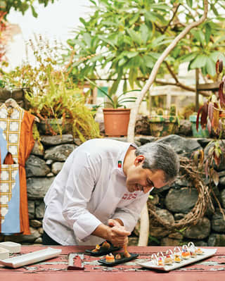 Chef in chef whites preparing canapes on an outdoor table next to a stone wall