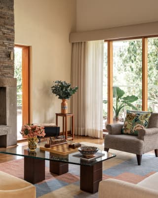 A sofa and two armchairs circle a rhombus glass-top table in the spacious living room, with a fireplace and window walls.