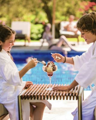 Two ladies in bathrobes at an outdoor poolside sharing an ice cream sundae