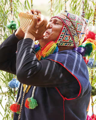 Traditional Peruvian shaman blowing a conch among brightly coloured hanging decorations