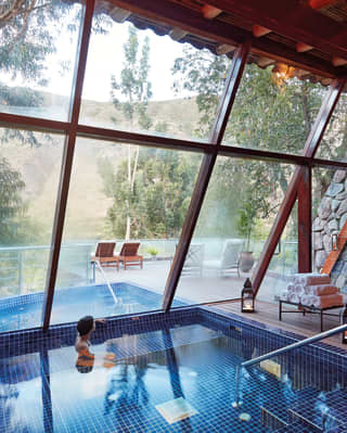 Lady swimming in a plunge pool with floor to ceiling windows overlooking the treetops of Sacred Valley