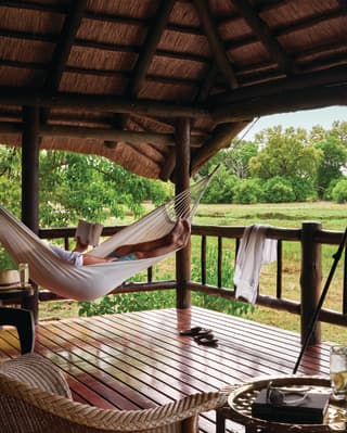 Lady relaxing in a hammock on a safari lodge terrace overlooking the savannah
