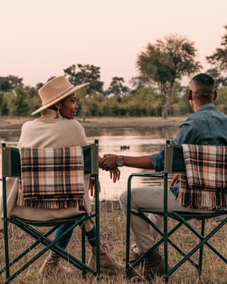 A couple sitting on canvas chairs and holding hands overlooking a watering hole