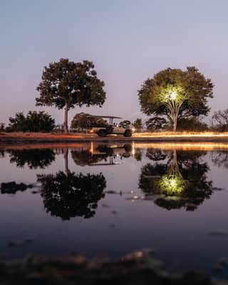 View across a still lake of a safari truck driving at sundown