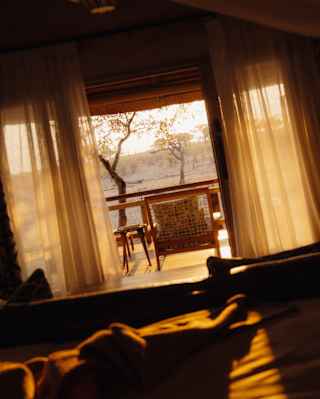 Angled image of a deck overlooking the plains, bathed in golden sun, seen through open drapes from a lodge interior.