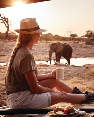 A guest enjoys her breakfast watching an elephant at the water hole nearby