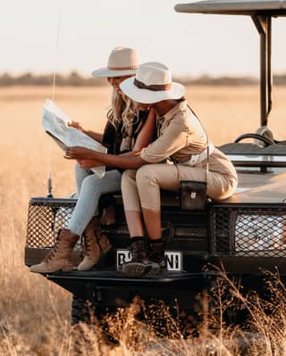 Two guests check a map while sitting on the front of the Belmond safari vehicle while out in the bush