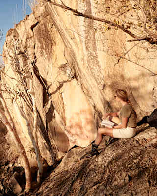 A guest sits on a sunny rock overlooking the bush