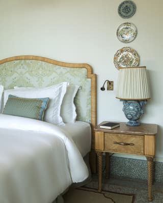 In a bedroom detail, white linen and cool blue furnishings are warmed with wood touches and a vintage table with turned legs.