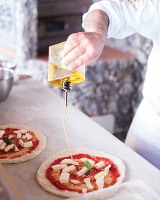 a chef making a pizza pouring olive oil