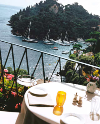 Angled view of the blue Baia Cannone, with boats lined along the headland, seen from a sunny table at La Terrazza restaurant.