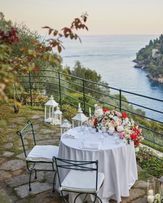 A bouquet of roses cascades over the edge of a table set for two in a private corner of the garden with unrivalled bay views
