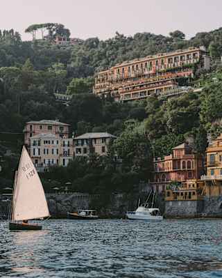 A single-sail boat drifts left of a view into Baia Cannone, overlooked by the magnificent Splendido hotel on a hill above.