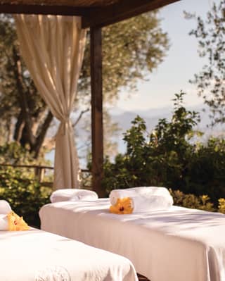 Twin treatment tables topped with fluffy white towels and large yellow hibiscus flowers enjoy dappled shade on the terrace