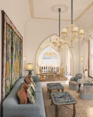 A blue sofa faces a row of full-height windows on to the sea in Villa Beatrice's living room, with adjoining dining room.