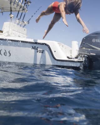 Lady in an orange swimsuit diving from a boat into clear waters
