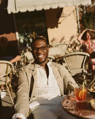 Hombre sonriente bebiendo un cóctel en una mesa de restaurante al aire libre