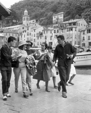 A group of young friends are walking quickly and talking animatedly on Portofino's harbour wall  in this black and white image