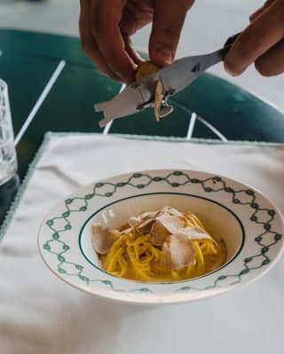 close up of pair of hands shaving white truffles ove a pasta dish