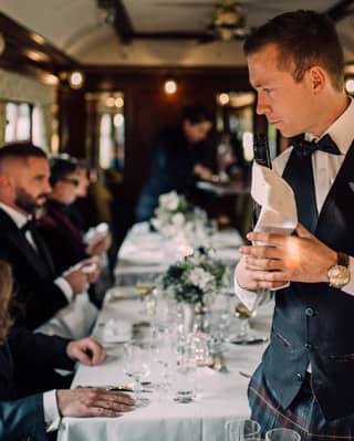 Steward in a waistcoat and bow tie polishing glasses