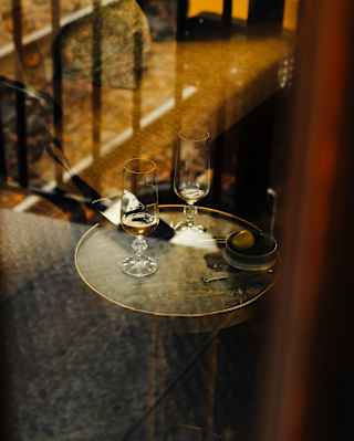 Two tasting glasses, each with a nip of whisky, rest on a round side table, viewed through a glass-panelled window.