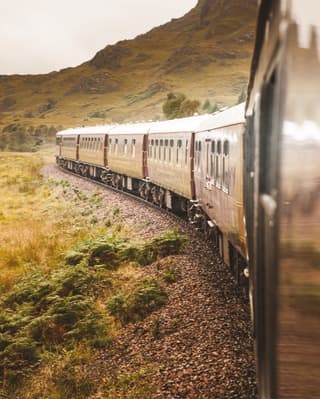 Gleaming burgundy carriages of Royal Scotsman curving through a Scottish glen.