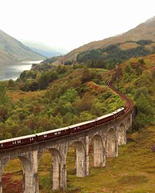 Aerial view of The Royal Scotsman as it crosses the Glenfinnan Viaduct on a damp and misty day, with views of Loch Shiel.