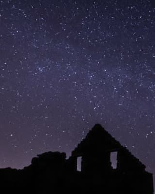 Above the silhouette of a ruin, stars spray across a purple night sky, seen in an expert-led astronomy tour in the Cairngorms.