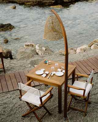 A arc standing lamp with wicker shade stands over a waterside dining table laid for two guests at Brizza, seen from above.