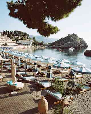 Rows of blue and white parasols and loungers follow the sweep of Mazzarò Bay in a beautiful image of Lido Villeggiatura.
