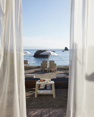 View through linen drapes of sunbeds under a white parasol on a shoreline