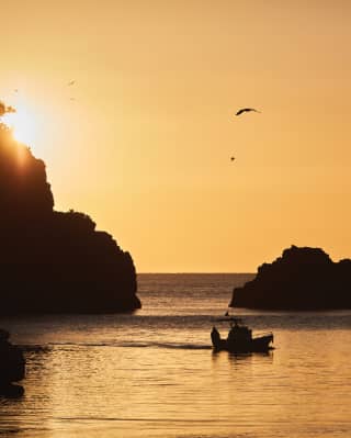 Silhouette of a sailing boat sailing in a rocky bay in an orange sunset