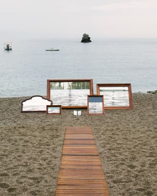 A cane beach mat creates a path across the course grained sand to an art installation of six framed pictures of the sea