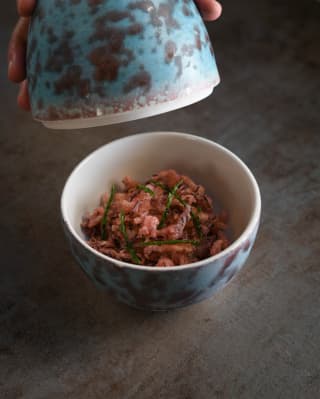 Close-up of a blue marble egg-shaped bowl containing pink crisped squid and samphire