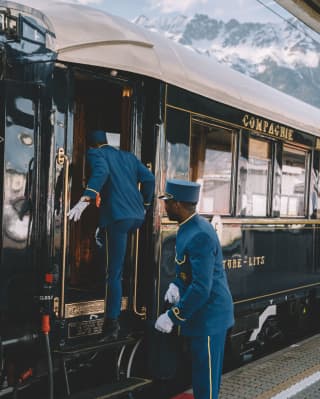 Dos camareros vestidos de azul subiendo a un tren de lujo