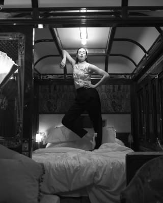 Black and white photo of a lady standing on a double bed