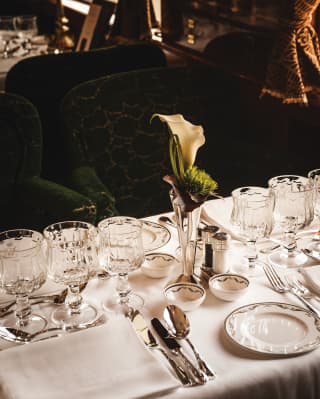 A single Arum lily in a silver bud vase sits centre of a table set for four, with exclusive glassware and porcelain plates