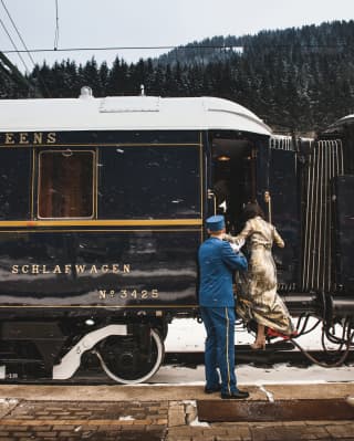 Camarero del tren con un uniforme azul ayudando a una señora a subir a un vagón azul