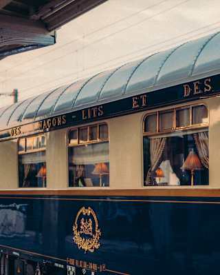The cream, blue and gold livery of the dining car's exterior shines in the early evening sun. Inside table lamps glow orange